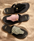 Black sandals with various embellishments on a beige surface