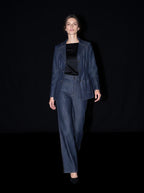 A model walks against a black background wearing a matching dark blue denim jacket and wide-leg jeans, styled with a black top and black shoes.