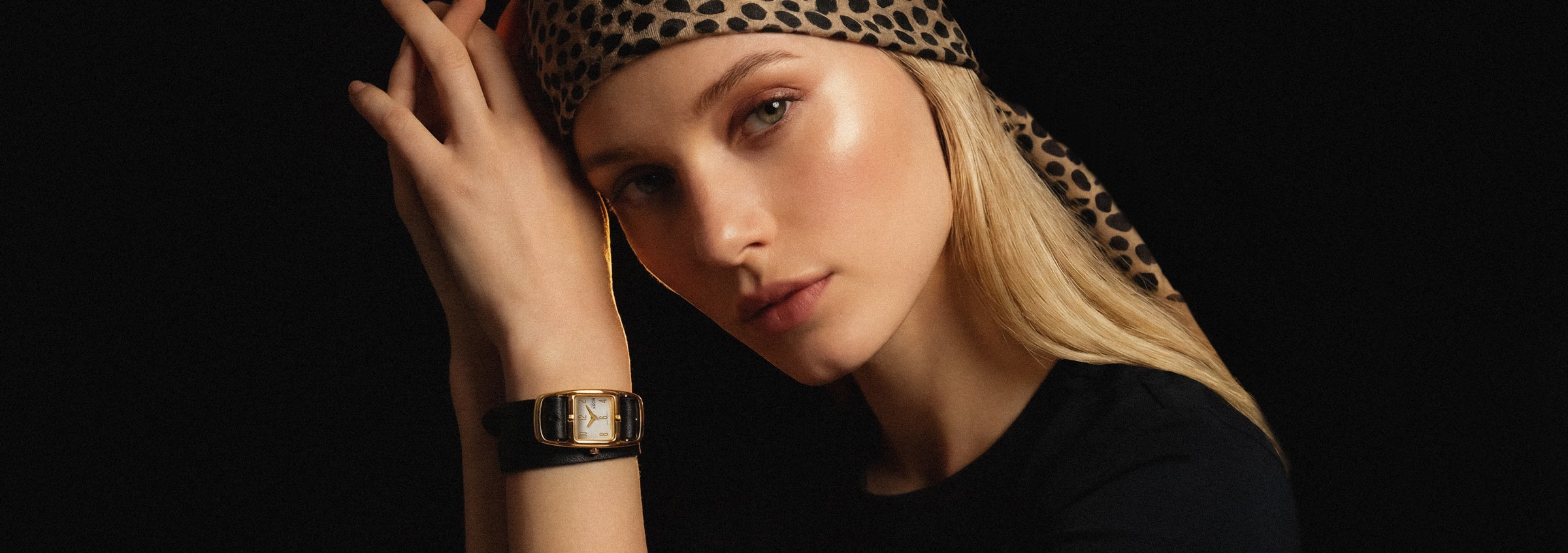 Woman wearing a leopard print headband and black watch against a dark background