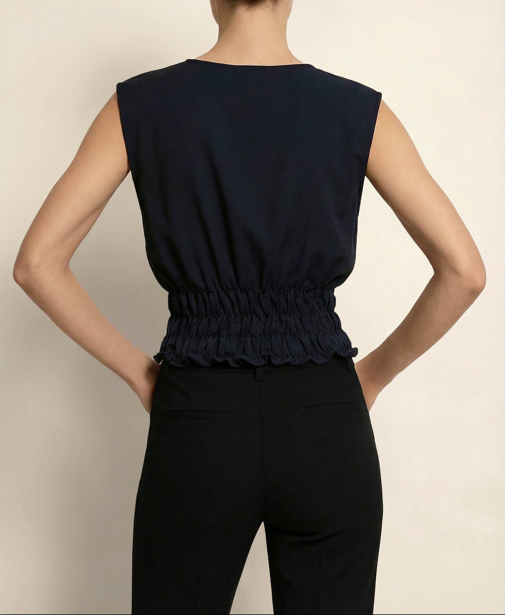 Woman wearing a blue holborn sleeveless top with a ruffled hem against a beige background by isabella kron