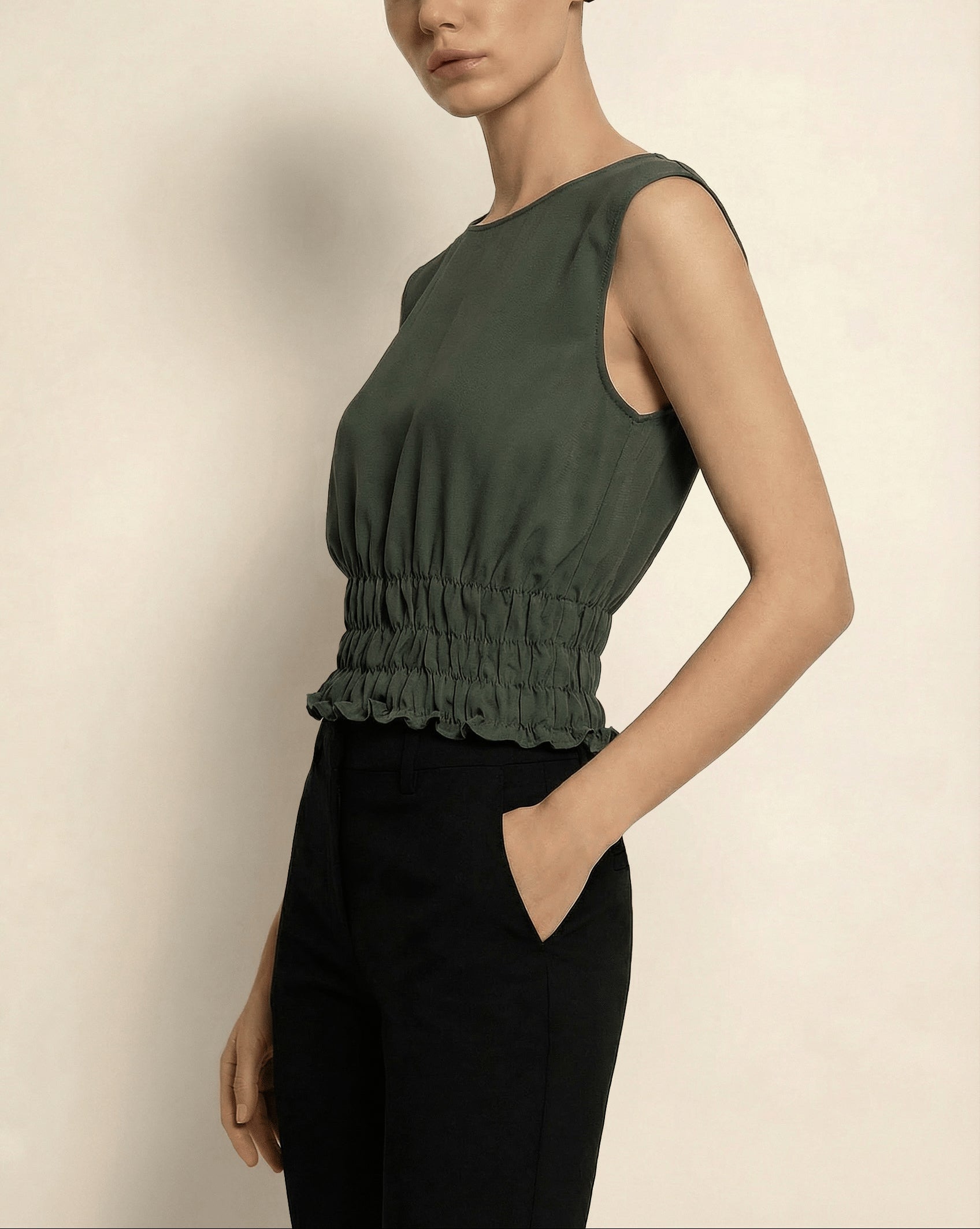 Woman wearing a green holborn sleeveless top with a ruffled hem against a beige background by isabella kron