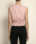 Person wearing a pink sleeveless top and black pants against a beige background