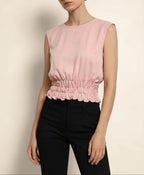 Woman wearing a pink sleeveless top and black pants against a beige background