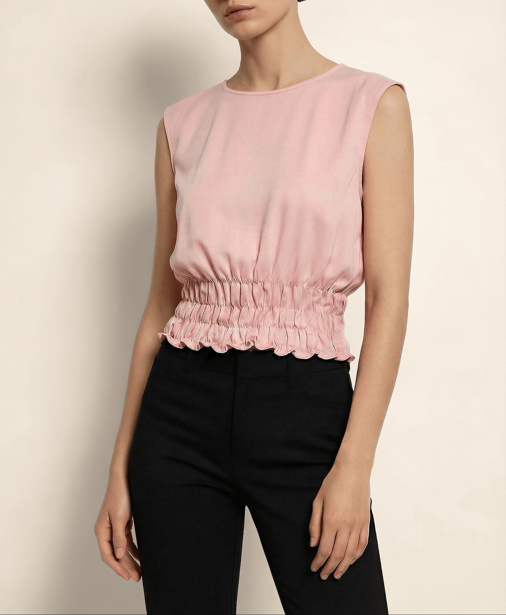 Woman wearing a pink sleeveless top and black pants against a beige background