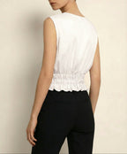 Woman wearing a white sleeveless top with a scalloped hem and black pants against a beige background