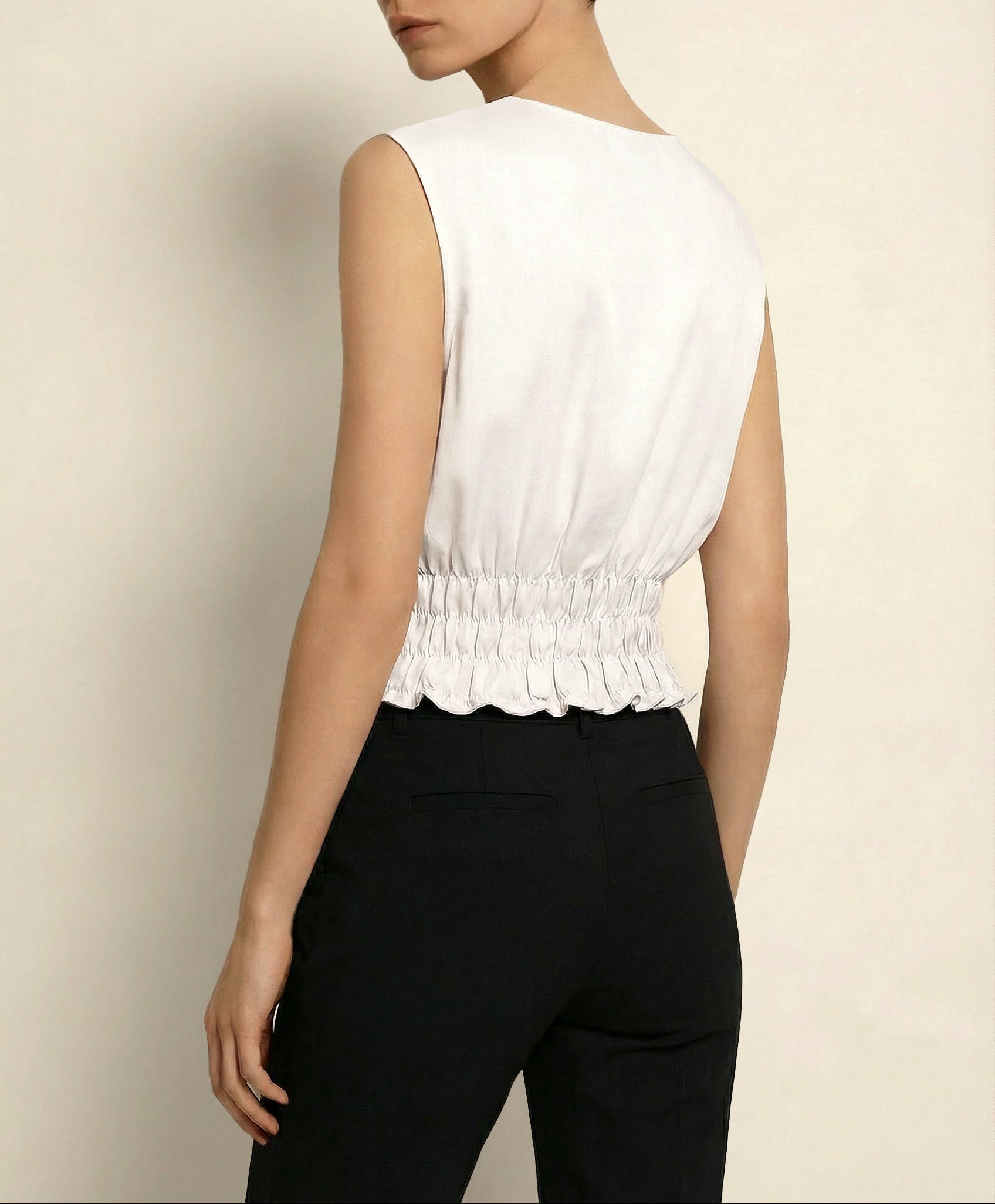 Woman wearing a white sleeveless top with a scalloped hem and black pants against a beige background