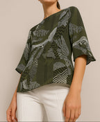 Person wearing a green patterned top with white pants on a beige background