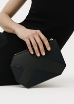 Black geometric leather clutch bag with gold zipper held by model in black dress — sculptural angular evening clutch luxury accessory close-up