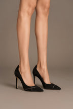 Model wearing Isabella Kron Miriam Black Suede Pump, showcasing slender stiletto heel and sculpted arch silhouette in rich black suede
