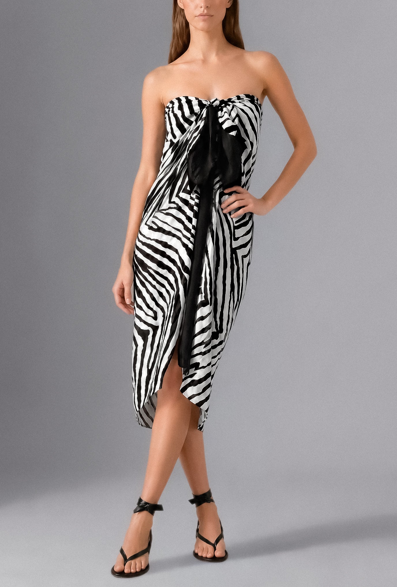 Woman wearing the Savana Pareo in white and black graphic print styled as a lightweight luxury beach wrap