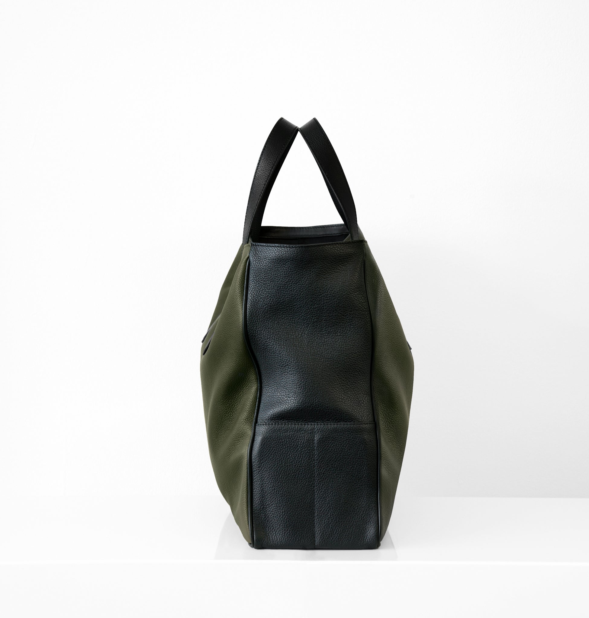 Side view of Isabella Kron Leo Shopper in military green, showing slim folded profile, reinforced bottom and black leather handles