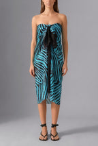 Woman wearing the Savana Pareo in turquoise and black graphic print styled as a lightweight luxury beach wrap over swimwear
